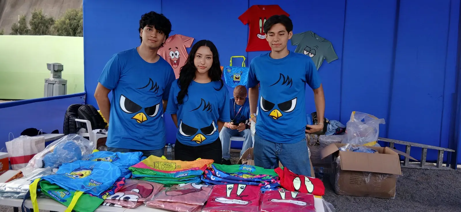 Equipo del evento frente a una exhibición de camisetas y bolsas de Bob Esponja